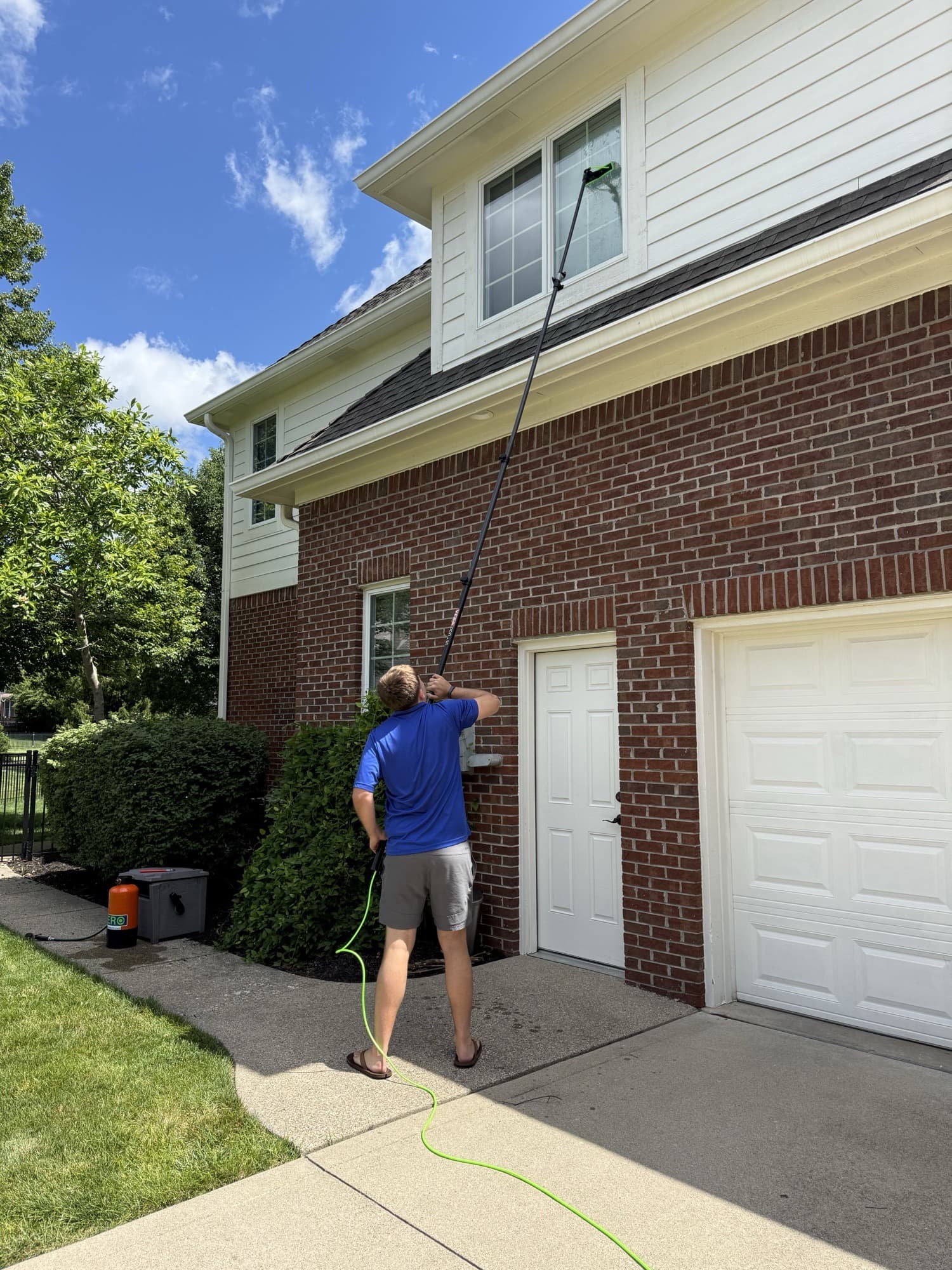 Squeegee Guys technician cleaning a second-story window with a water-fed pole